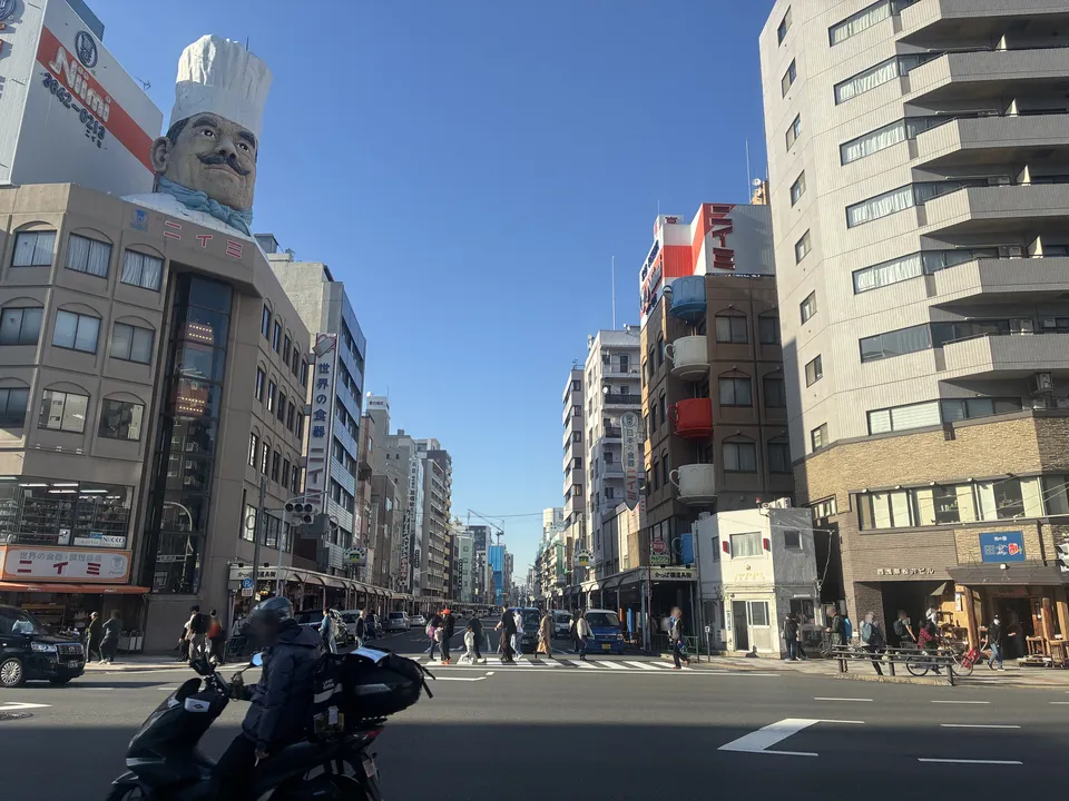 Kappabashi Dougu Street seen from the main intersection on a clear day, with the giant chef figure on the Niimi building at the top left and the street running ahead lined with kitchenware shops