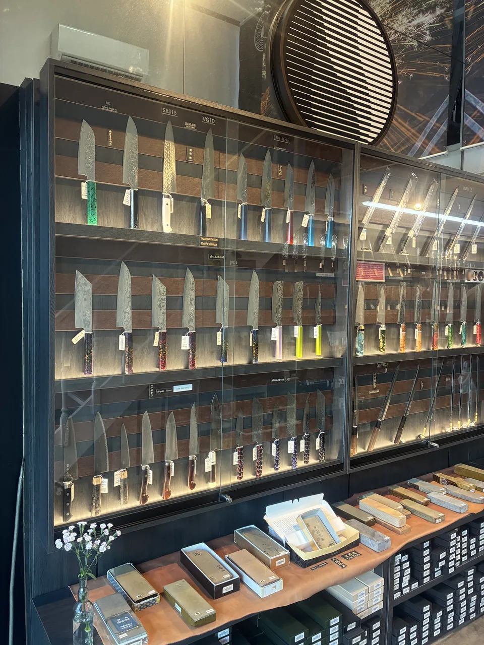 A glass display case filled with rows of Japanese kitchen knives with colorful handles including teal, yellow, red, and purple at a Kappabashi knife shop