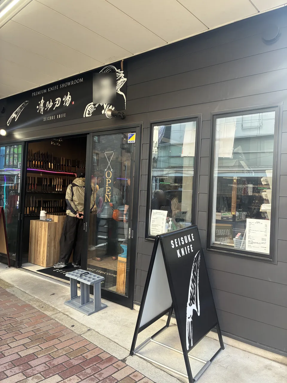 The SEISUKE KNIFE storefront in Kappabashi seen from a low angle, showing the 清助刃物 (Seisuke Hamono) overhead panel and a display window filled with knives