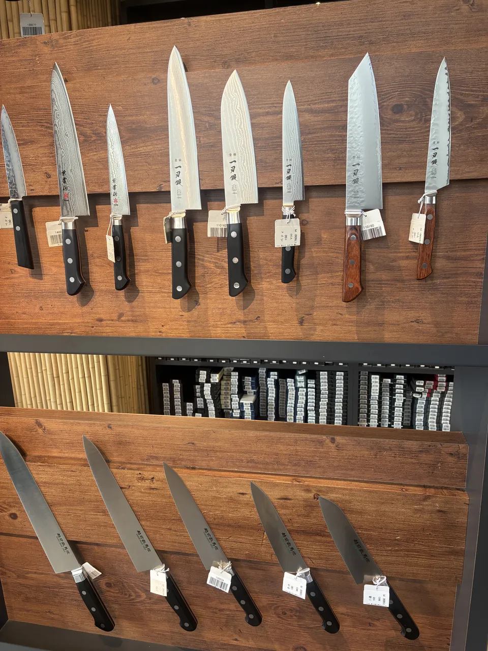 Japanese kitchen knives of various sizes mounted on two wooden display boards at a Kappabashi knife shop, ranging from large chef's knives to small paring knive