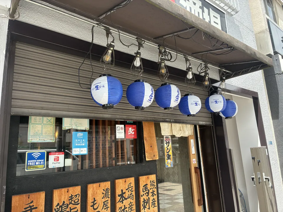 The entrance of an Asakusa izakaya with five blue and white round paper lanterns and wooden menu boards advertising 熊本産 馬刺 (Kumamoto horse sashimi) and other sp