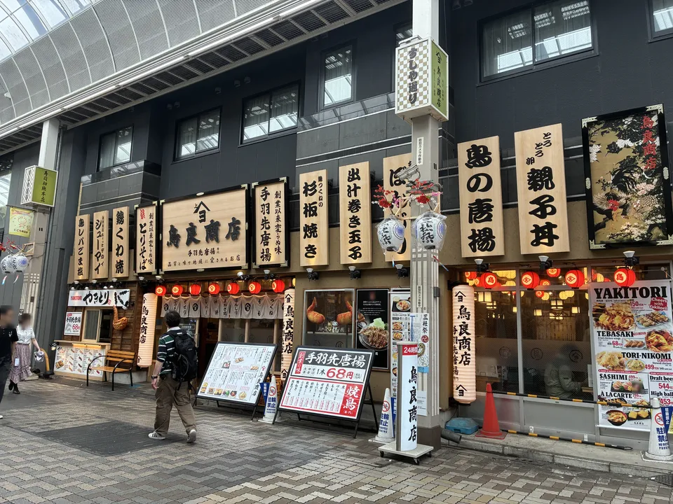 The facade of 今井鳥良商店 (Imai Toriyoshi Shoten) inside a covered arcade in Asakusa, with wooden hanging signs reading 手羽先唐揚 (chicken wing karaage), 杉板焼き (cedar pla