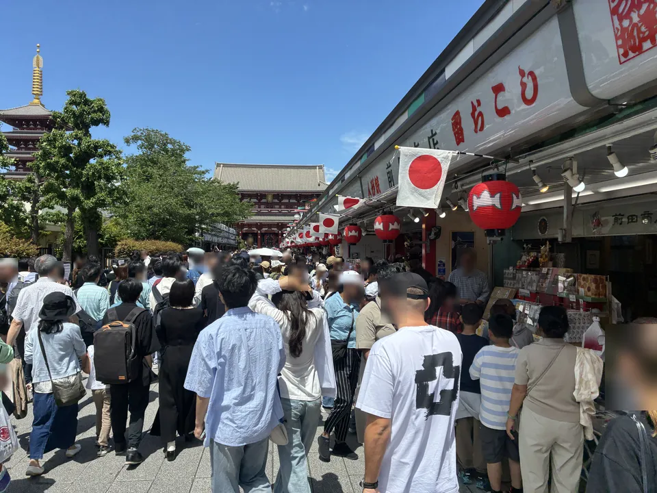 Nakamise-dori looking toward the Hozomon Gate of Senso-ji with dense festival crowds, Japanese national flags and red lanterns, the five-story pagoda visible to