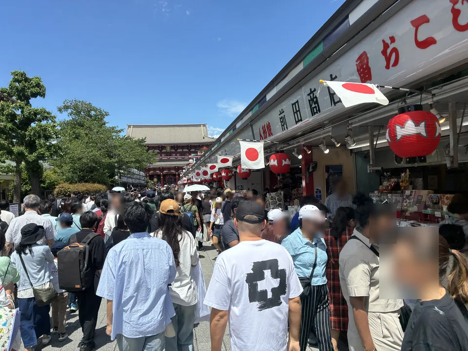 Nakamise-dori looking toward Senso-ji's Hozomon Gate with dense festival crowds, Japanese national flags and red lanterns decorating souvenir shops including a