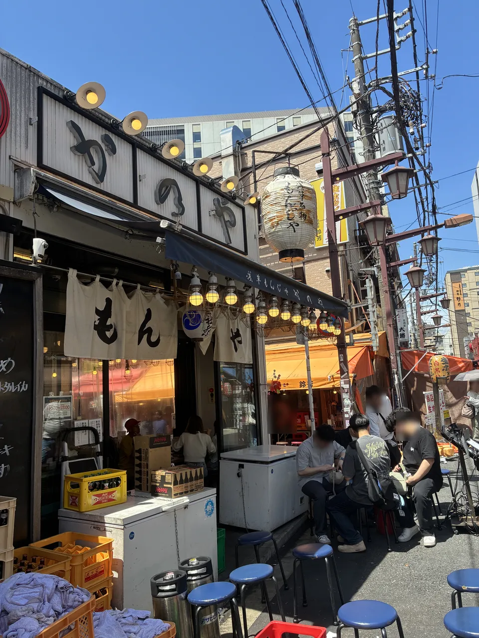 Rotated view of a restaurant in Asakusa with a large overhead yellow paper lantern, additional small yellow lanterns along the awning, large calligraphic sign p
