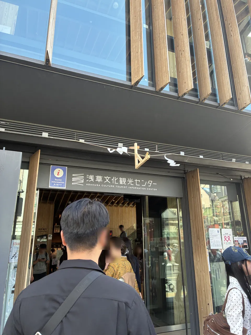 Rotated close-up of the entrance to 浅草文化観光センター (Asakusa Culture Tourist Information Center), a modern building with wooden slatted exterior, a musical staff mot