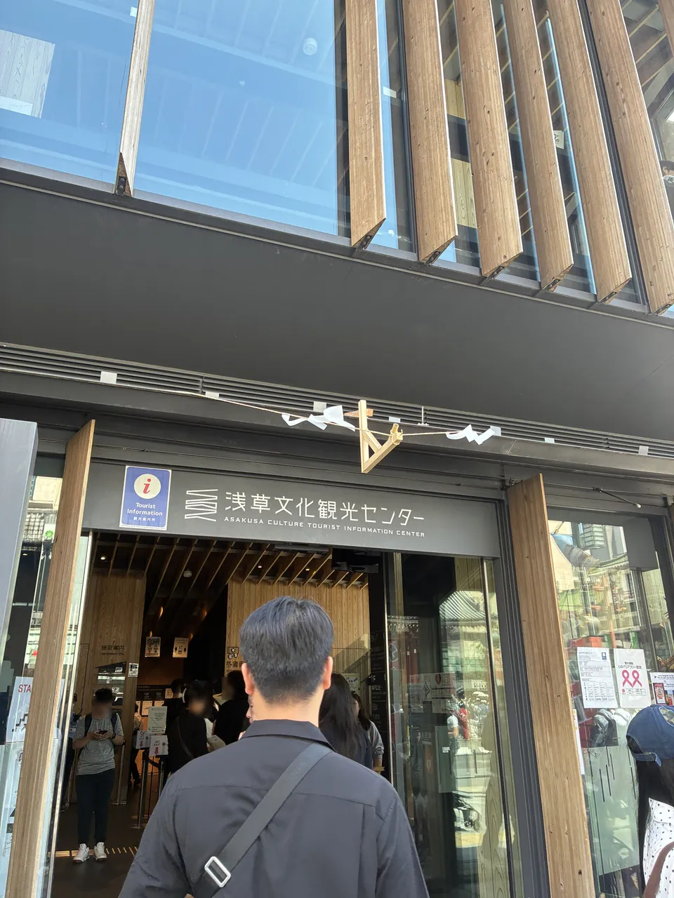 The entrance facade of 浅草文化観光センター (Asakusa Culture Tourist Information Center) with a modern wooden slatted exterior, the center's name sign visible on the glas
