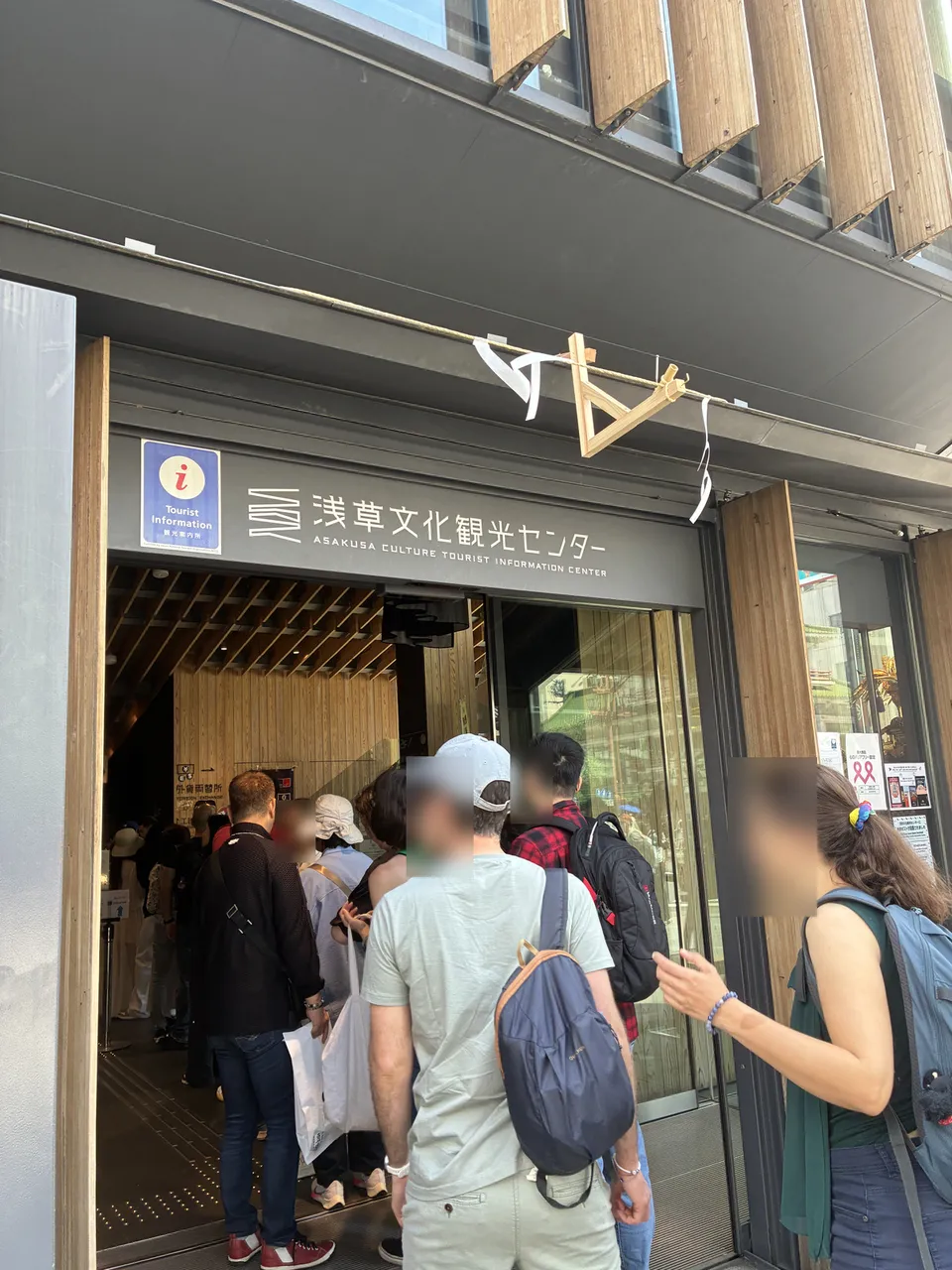 Rotated exterior of 浅草文化観光センター (Asakusa Culture Tourist Information Center) showing the modern wooden slatted facade, overhead tourist information ⓘ sign, and v