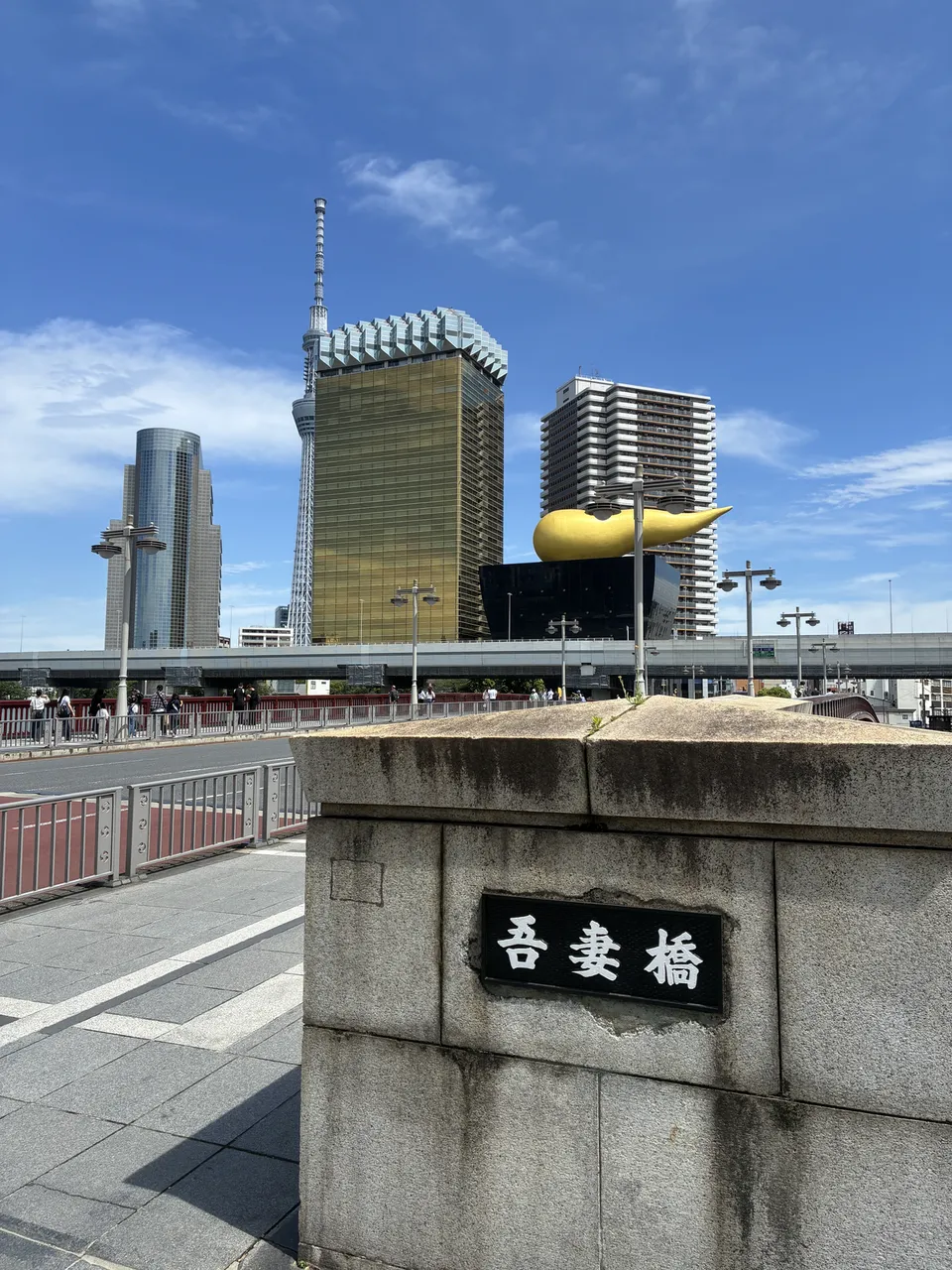 Rotated view from the 吾妻橋 (Azumabashi) bridge showing the gold Flamme d'Or sculpture on the Asahi Beer Hall, the Asahi Beer Tower, and a concrete bridge abutmen