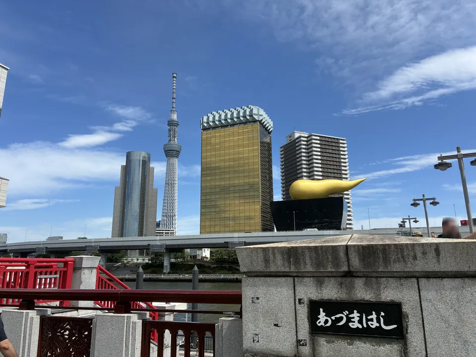 The あづまはし (Azumabashi) nameplate on a stone bridge abutment with the Sumida River skyline behind it showing Tokyo Skytree, the Asahi Beer Tower, and the gold Fl