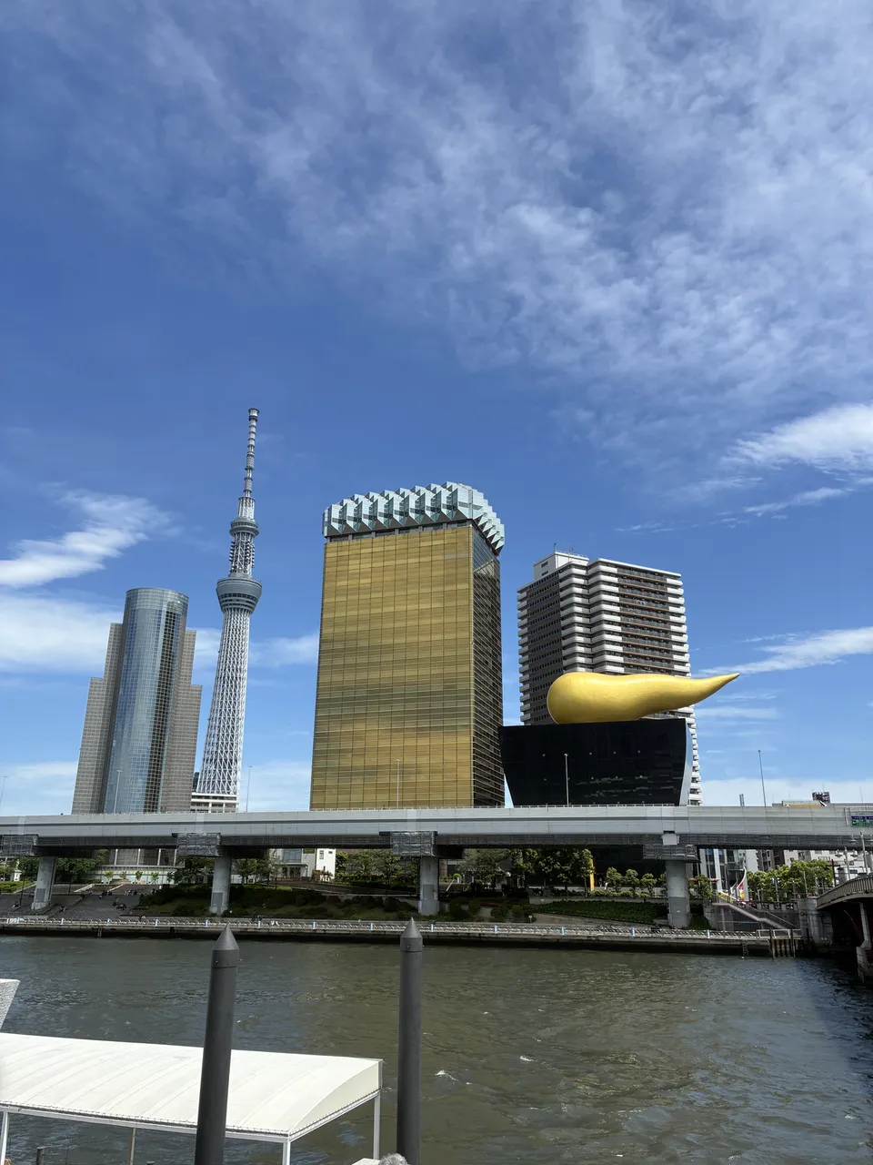 Rotated view across the Sumida River from the Azumabashi area showing Tokyo Skytree at center-left and the Asahi Beer Tower with the gold Flamme d'Or sculpture 