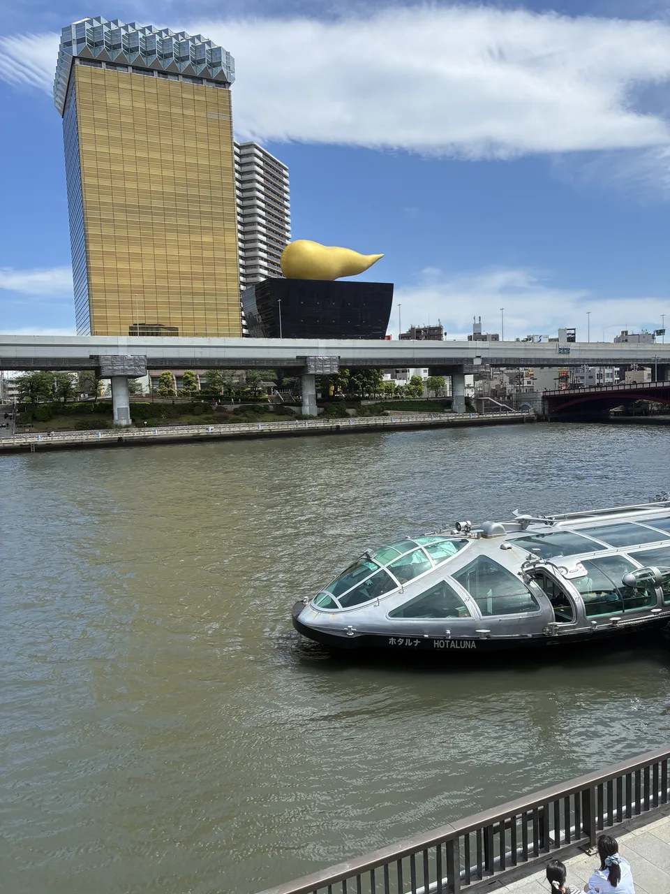 The silver HOTALUNA water bus on the Sumida River with the Asahi Beer Tower and gold Flamme d'Or on the left