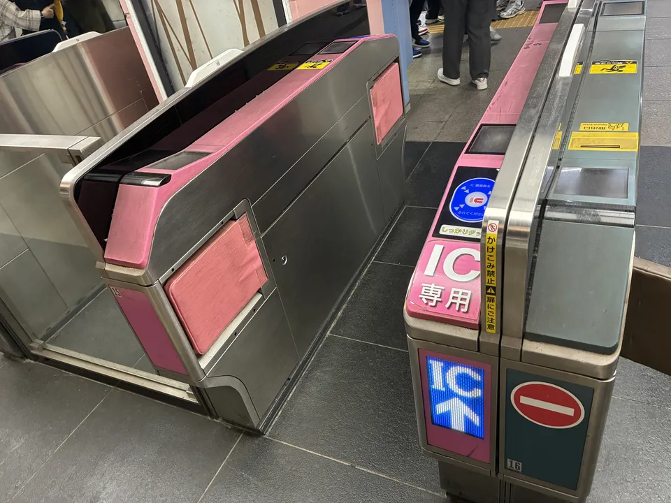 A wide ticket gate with pink panels and a sign reading IC 専用, meaning IC cards only, next to a standard gate