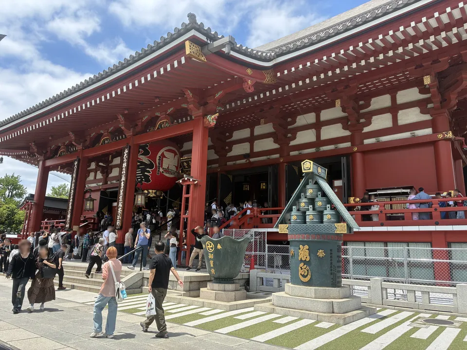 The main hall of Senso-ji in Asakusa with its red pillars and giant lantern, with the green-roofed bronze incense burner and a lotus-shaped water basin in front of the steps